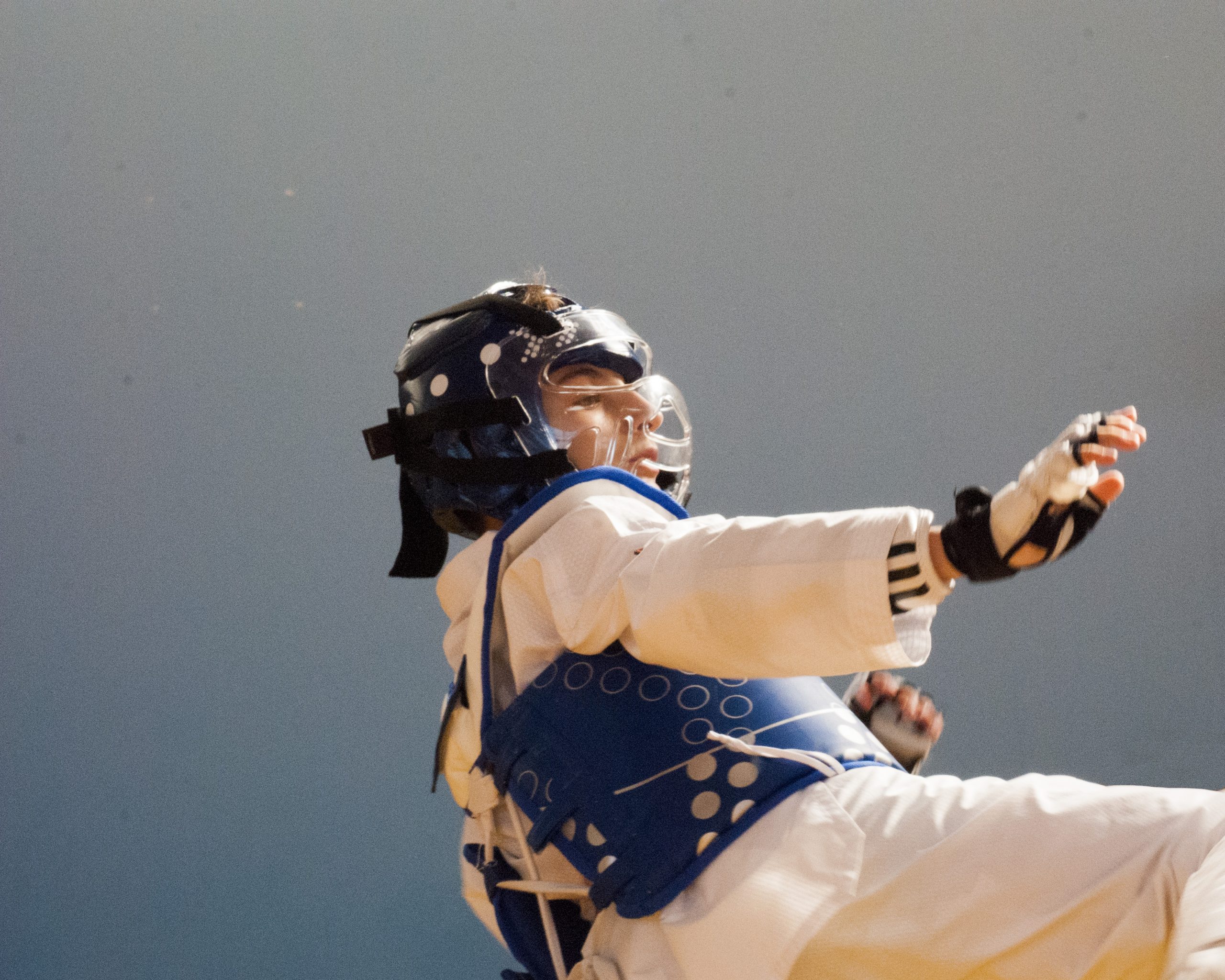 Un jeune taekwondoiste avec ses protection fait un mouvement technique sur fond bleu